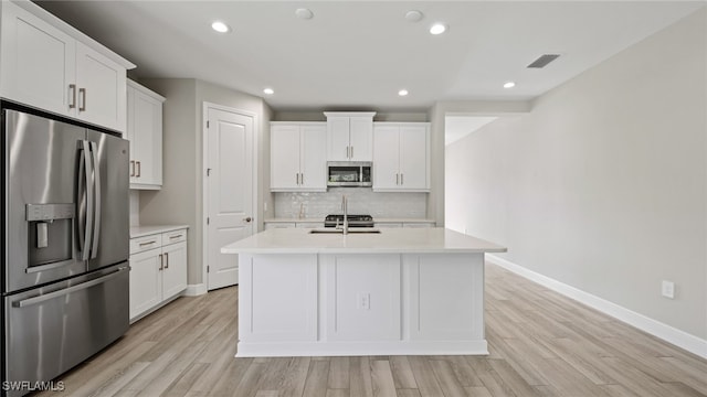 kitchen featuring light wood-type flooring, white cabinets, an island with sink, appliances with stainless steel finishes, and decorative backsplash