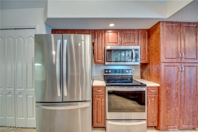 kitchen with stainless steel appliances, brown cabinetry, and light countertops