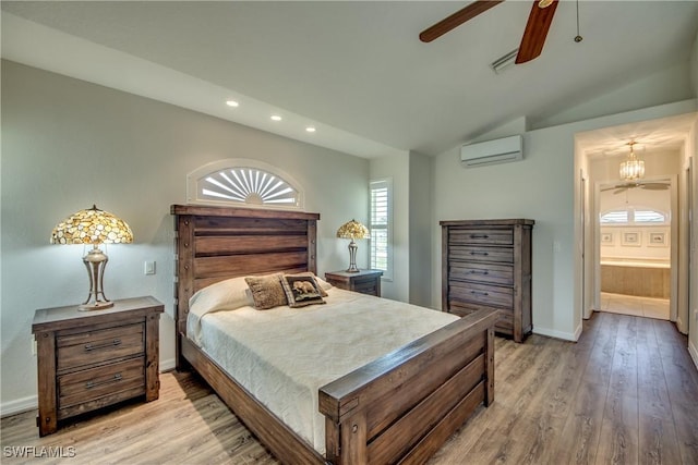 bedroom featuring light wood finished floors, baseboards, connected bathroom, a wall unit AC, and vaulted ceiling