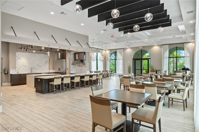 dining space featuring light wood-type flooring, sink, a wealth of natural light, and coffered ceiling