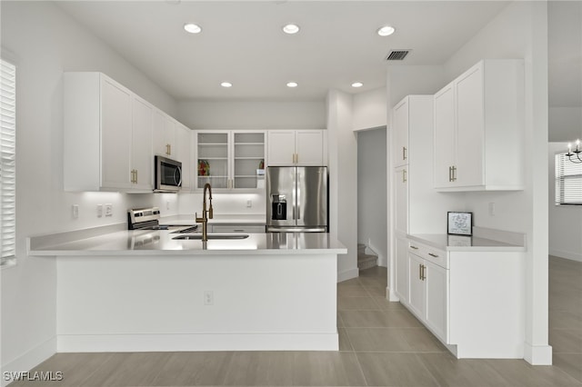 kitchen with kitchen peninsula, appliances with stainless steel finishes, sink, white cabinets, and light tile patterned flooring