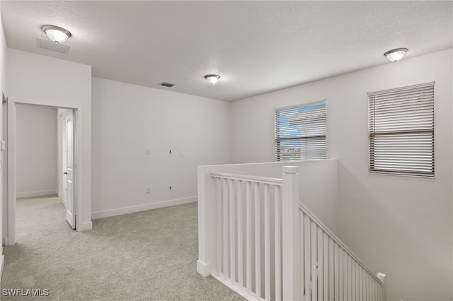 hall with light colored carpet and a textured ceiling