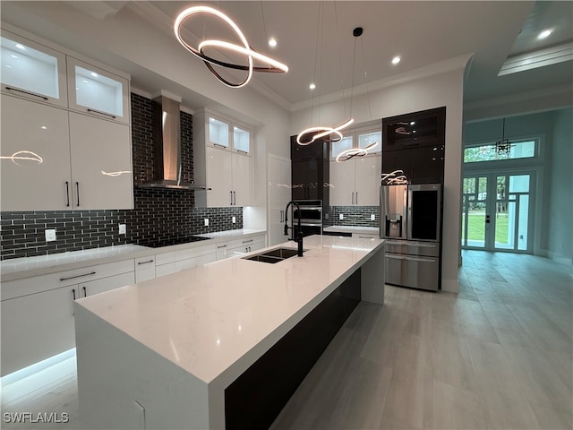 kitchen with a kitchen island with sink, pendant lighting, wall chimney range hood, and appliances with stainless steel finishes