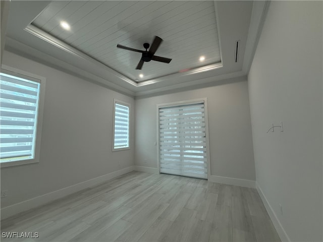 empty room featuring a tray ceiling, ceiling fan, and light hardwood / wood-style flooring