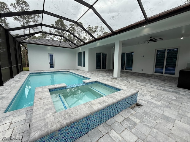 view of pool featuring glass enclosure, an in ground hot tub, ceiling fan, and a patio