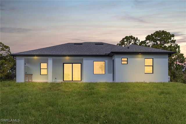 back house at dusk featuring a yard