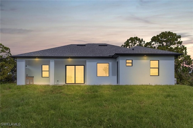 1220 Edison Ave, Lehigh Acres, FL 33972 - back of property at dusk featuring a yard, roof with shingles, and stucco siding