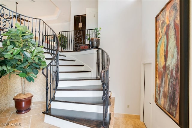 stairway featuring tile patterned floors, a raised ceiling, and a towering ceiling