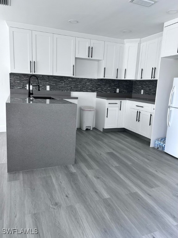 kitchen with hardwood / wood-style floors, white fridge, decorative backsplash, and white cabinetry