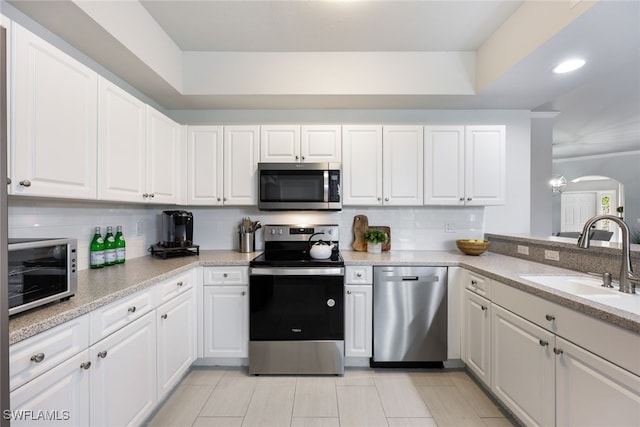 kitchen with stainless steel appliances, sink, white cabinets, a tray ceiling, and decorative backsplash