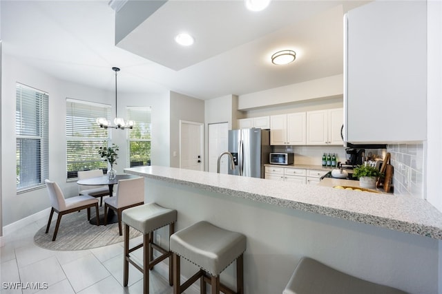 kitchen featuring a chandelier, appliances with stainless steel finishes, white cabinetry, light tile patterned flooring, and backsplash