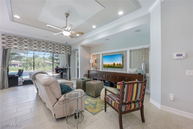 living room featuring ceiling fan, a raised ceiling, and ornamental molding