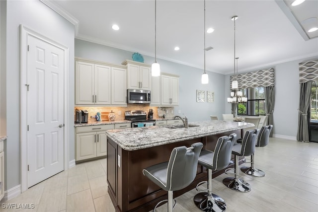 kitchen featuring light stone counters, pendant lighting, an island with sink, and appliances with stainless steel finishes