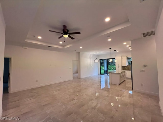 unfurnished living room with a raised ceiling, baseboards, visible vents, and ceiling fan