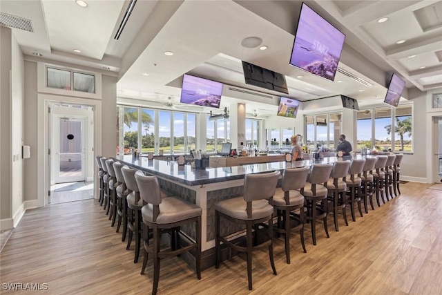 bar featuring coffered ceiling, beam ceiling, a high ceiling, and light wood-type flooring