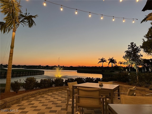 patio terrace at dusk featuring a water view and outdoor dining space