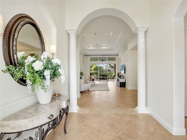 hallway with baseboards, a tray ceiling, light tile patterned floors, and ornate columns