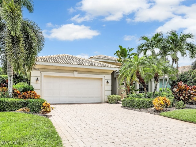 view of front facade with a tiled roof, decorative driveway, an attached garage, and stucco siding