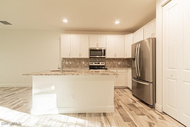 kitchen with appliances with stainless steel finishes, light stone counters, a kitchen island with sink, sink, and white cabinets