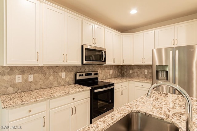 kitchen featuring white cabinets, light stone countertops, backsplash, and appliances with stainless steel finishes