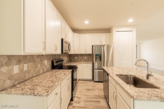 kitchen featuring white cabinetry, sink, light stone counters, appliances with stainless steel finishes, and light wood-type flooring