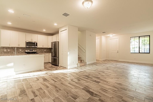 kitchen with light stone counters, appliances with stainless steel finishes, decorative backsplash, white cabinets, and light wood-type flooring