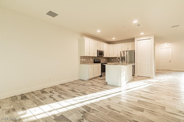 kitchen featuring white cabinets, appliances with stainless steel finishes, light wood-type flooring, and an island with sink