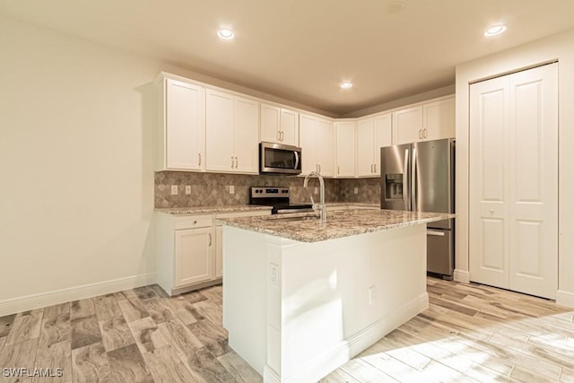 kitchen with stainless steel appliances, light stone counters, light hardwood / wood-style flooring, a center island with sink, and white cabinets