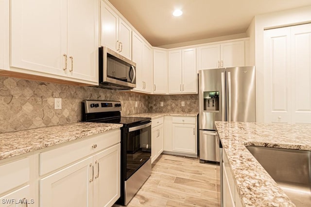 kitchen with appliances with stainless steel finishes, light hardwood / wood-style floors, white cabinetry, and light stone counters