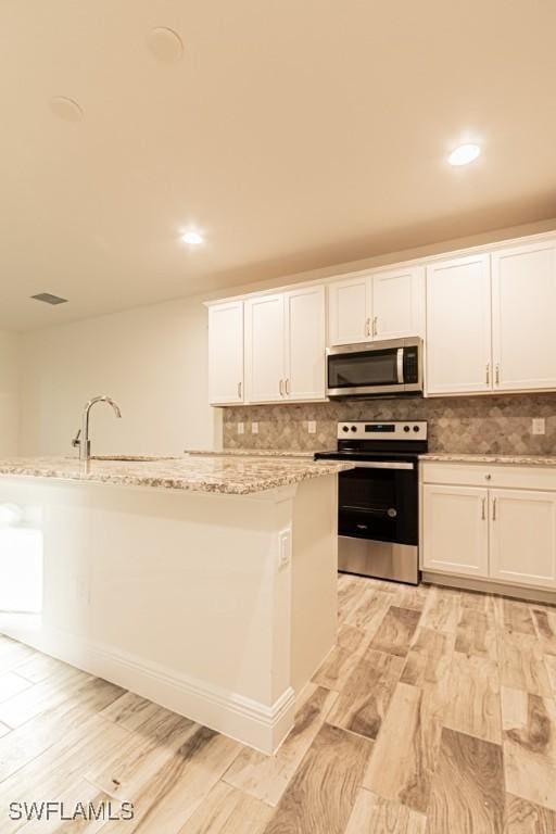 kitchen featuring white cabinetry, light stone countertops, stainless steel appliances, and tasteful backsplash