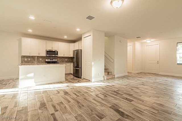 kitchen featuring an island with sink, white cabinets, light hardwood / wood-style floors, and appliances with stainless steel finishes