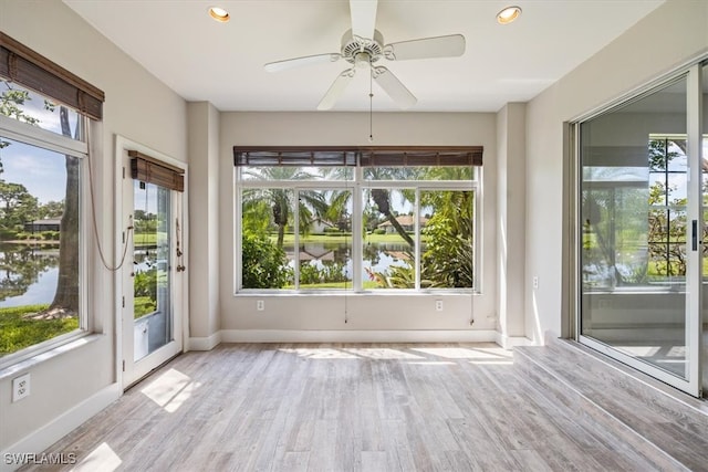 unfurnished sunroom featuring a water view, a healthy amount of sunlight, and ceiling fan