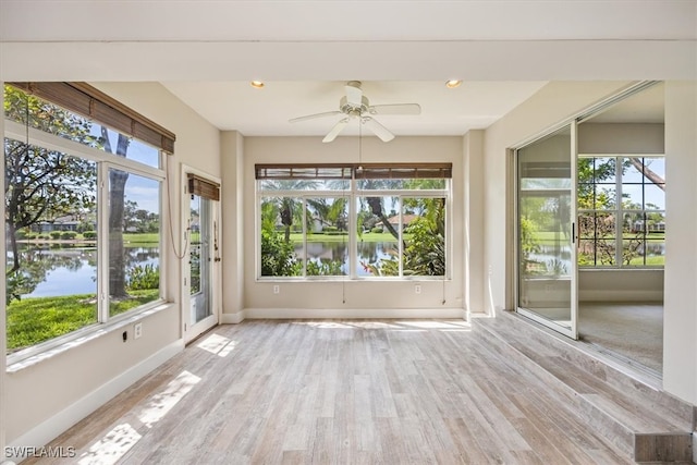 unfurnished sunroom with a healthy amount of sunlight, a water view, and ceiling fan