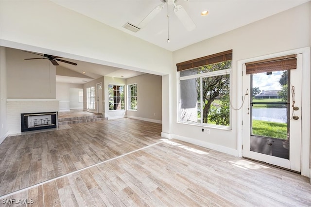 unfurnished living room with light hardwood / wood-style floors, lofted ceiling, a fireplace, and a water view