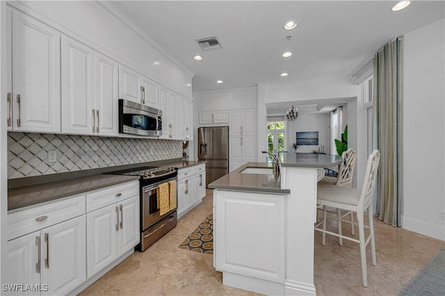 kitchen with appliances with stainless steel finishes, a center island with sink, white cabinets, a breakfast bar, and sink