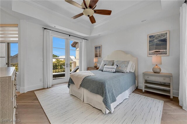 bedroom featuring light hardwood / wood-style flooring, ornamental molding, access to outside, a tray ceiling, and ceiling fan