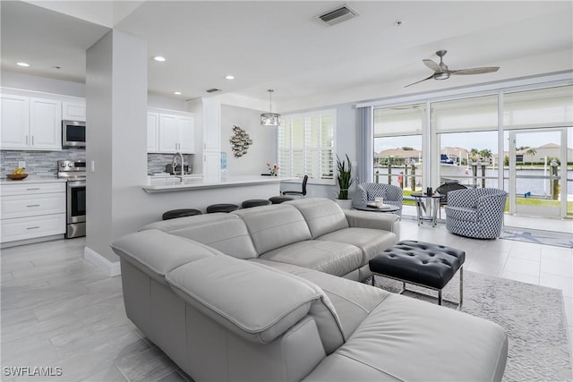 living area with a ceiling fan, recessed lighting, visible vents, and a water view