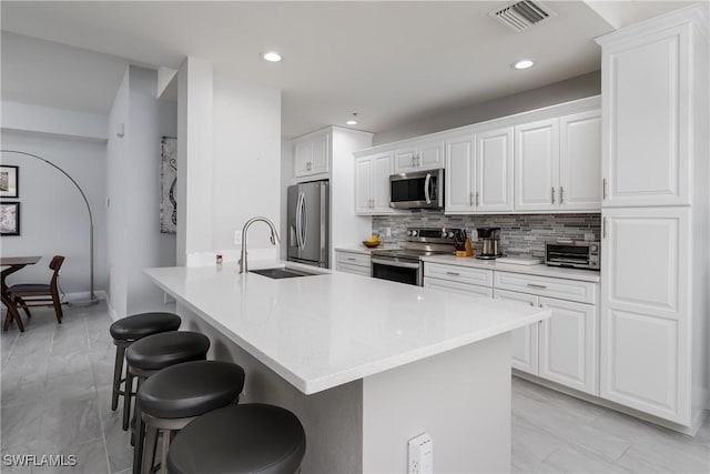 kitchen with tasteful backsplash, white cabinets, appliances with stainless steel finishes, a breakfast bar area, and light countertops