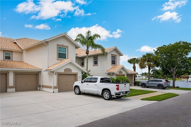 multi unit property with a garage, a tiled roof, concrete driveway, and stucco siding