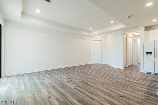 unfurnished living room with light wood-type flooring and a tray ceiling