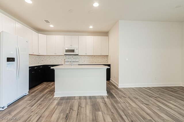 kitchen featuring white cabinets, light wood-type flooring, white appliances, and a kitchen island with sink