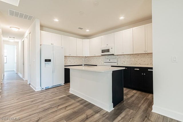 kitchen with backsplash, an island with sink, wood-type flooring, white appliances, and white cabinets