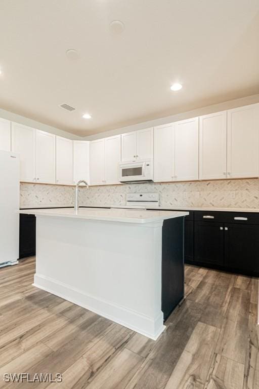 kitchen with a kitchen island with sink, light hardwood / wood-style floors, and white appliances