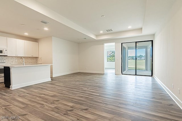 unfurnished living room featuring light hardwood / wood-style floors, a tray ceiling, and sink