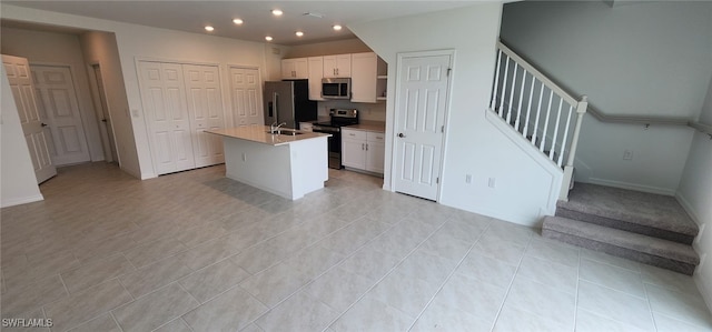 kitchen featuring light tile patterned floors, appliances with stainless steel finishes, an island with sink, sink, and white cabinetry