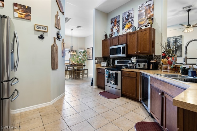 kitchen with light tile patterned flooring, sink, tasteful backsplash, hanging light fixtures, and stainless steel appliances