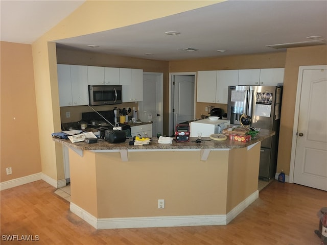 kitchen with appliances with stainless steel finishes, light hardwood / wood-style floors, a kitchen bar, and white cabinetry