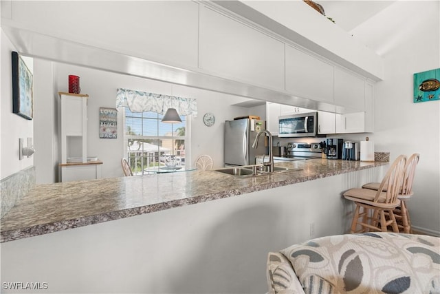 kitchen featuring stone counters, white cabinets, a kitchen breakfast bar, kitchen peninsula, and stainless steel appliances