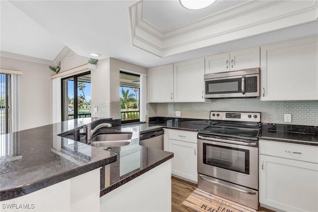 kitchen with dark stone countertops, stainless steel appliances, crown molding, white cabinets, and tasteful backsplash