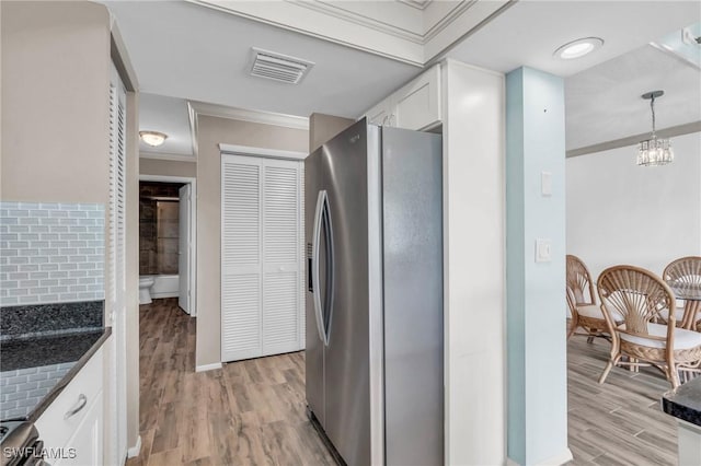 interior space featuring white cabinetry, hanging light fixtures, light hardwood / wood-style flooring, stainless steel fridge, and crown molding